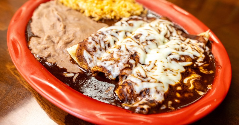 Enchiladas with Mole sauce, melted cheese, rice, and refried beans