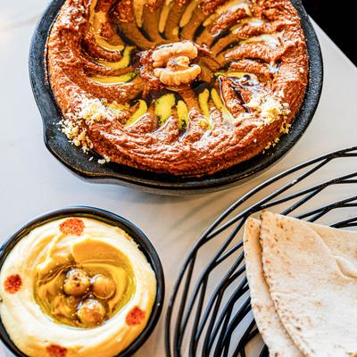 Roasted red pepper dip, hummus, and pita on a table.