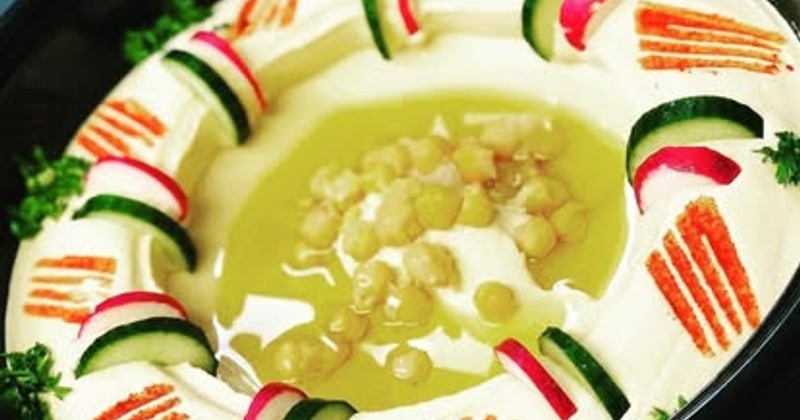 Hummus topped with olive oil, chickpeas, cucumber, and radish slices