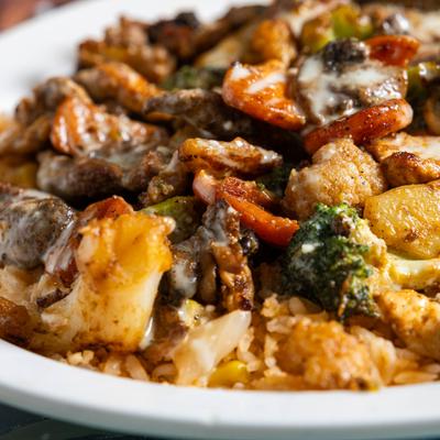 Bed of rice topped with chicken, steak, mixed vegetables, and cheese sauce.