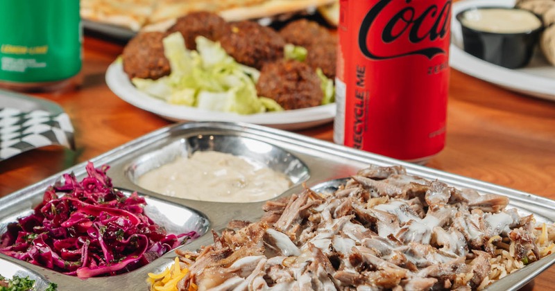 Beef shawarma plate on a table with assorted dishes and soft drinks, close up