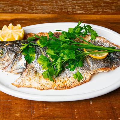 A grilled whole branzino garnished with parsley and lemon.
