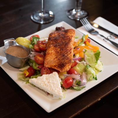 Salmon filet over a salad with cheese and dresssing.
