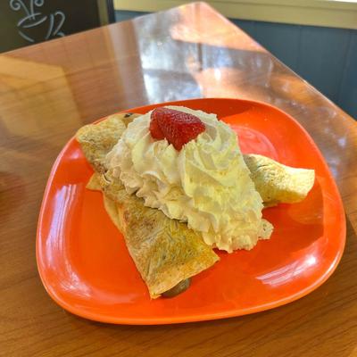 Crepes topped with whipped cream and a strawberry on an orange plate.