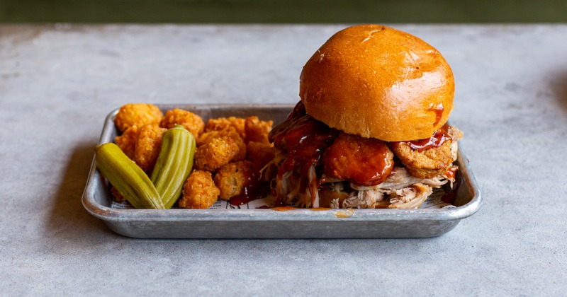 Pulled pork sandwich with pickle and tater tots on the side