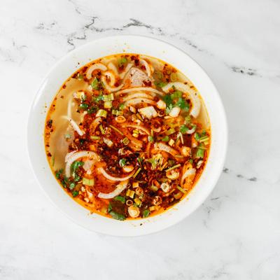 Spicy pho in a white bowl sits on a white marble table.