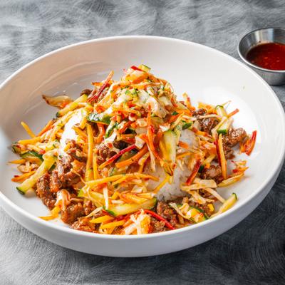 Steak Bowl with rice and varios vegetables, alongside a dressing.