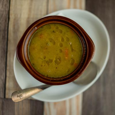 Bowl of soup, placed on a white dish with a spoon.