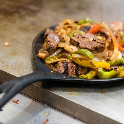 Sizzling steak fajitas with grilled peppers and onions served in a cast-iron skillet.