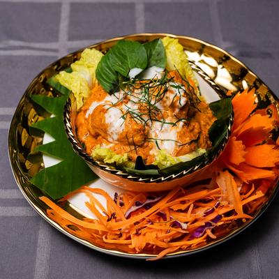 A bowl holds creamy orange curry with leafy greens, surrounded by carved carrots.
