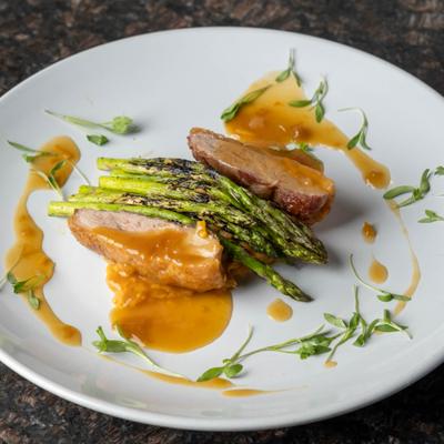 Duck breast with orange sauce and asparagus on a white plate.