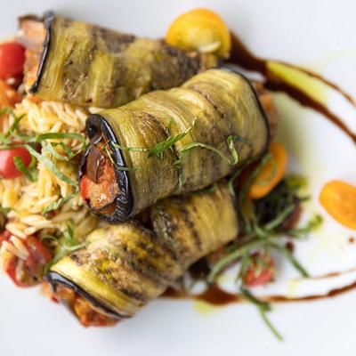 Eggplant rolls stuffed with vegetables served over orzo pasta.
