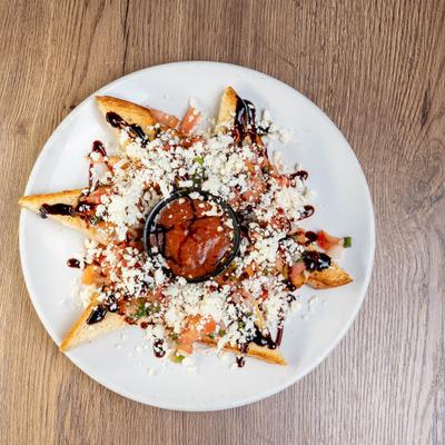 Bruschetta plate with a cup of red sauce in the center, set on a wooden table.