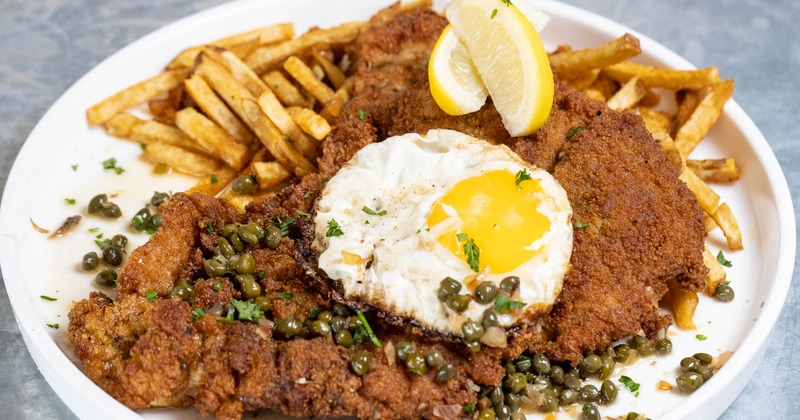 Weiner Schnitzel topped with fried egg and served with fries and lemon wedges
