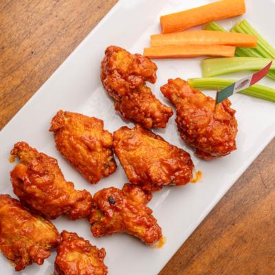 Buffalo wings served on a white plate with celery and carrot sticks.