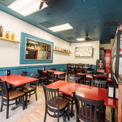 Restaurant interior featuring red tables, cushioned chairs, and pasta containers on a wooden shelf.