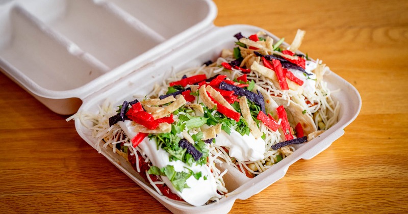 Tacos topped with tortilla strips and shredded cheese in a takeout container