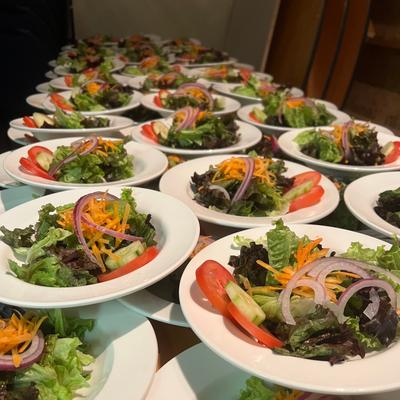Plates of mixed green house salads arranged in multiple rows.