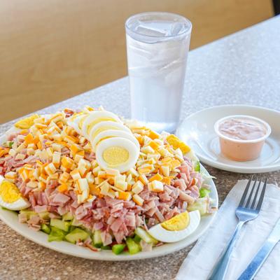 Chef salad topped with ham, cheese and boiled eggs, served with dressing and a drink.