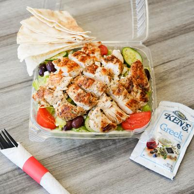 Buffalo chicken tenders over garden salad in a to go container.