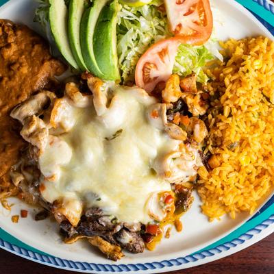 Grilled meat topped with melted cheese, served with beans, lettuce, tomato, avocado and rice