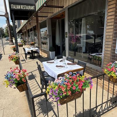 Street-side outdoor dining setup featuring a small table dressed with a white tablecloth.