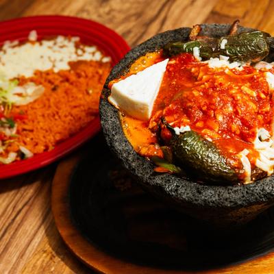A bowl of molcajete with cheese, salsa, and jalapenos, served with rice.