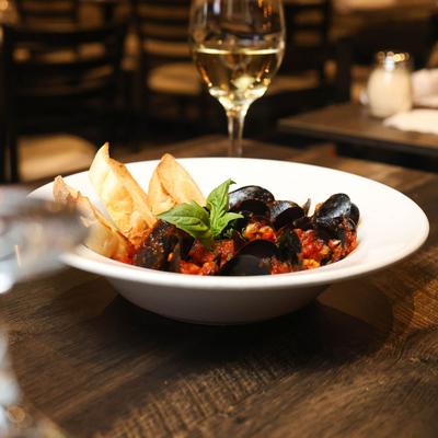 Mussels in tomato sauce with basil and toasted bread, paired with a glass of white wine.