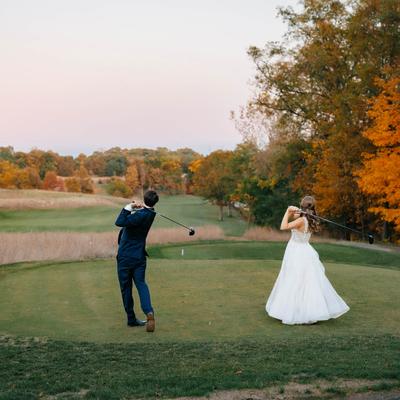 Newlyweds swing golf clubs together on a scenic course during fall.
