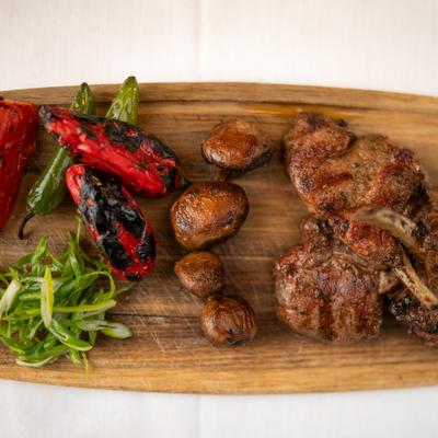 Seared lamb chops served with mushrooms and roasted peppers on a wooden board.