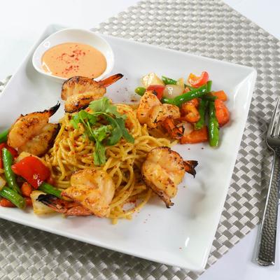 A plate of noodles with grilled shrimp, mixed veggies, and sauce on the side.