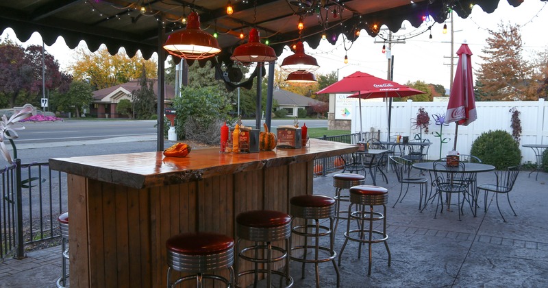 Outdoor patio with a wooden bar and red stools and string lights