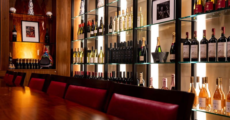 Interior, long tables with chairs and shelves with wine bottles
