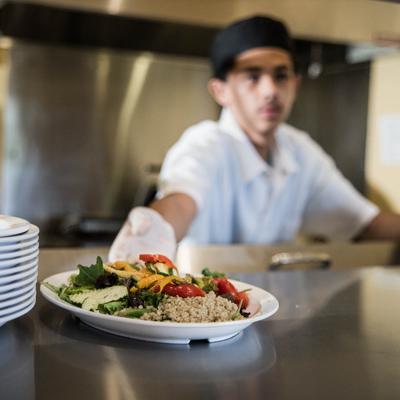 A cook presenting a salad with mixed greens, quinoa, and beets.