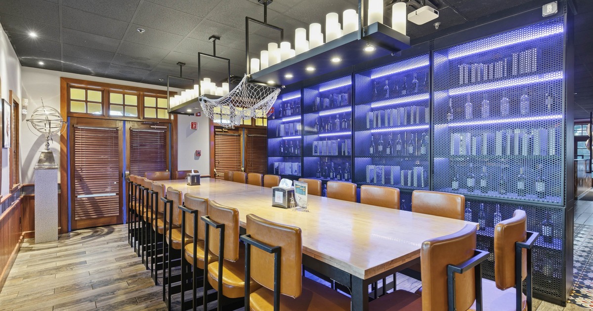 Dining area with a long wooden table, leather chairs, decorative netting, and backlit bottle display