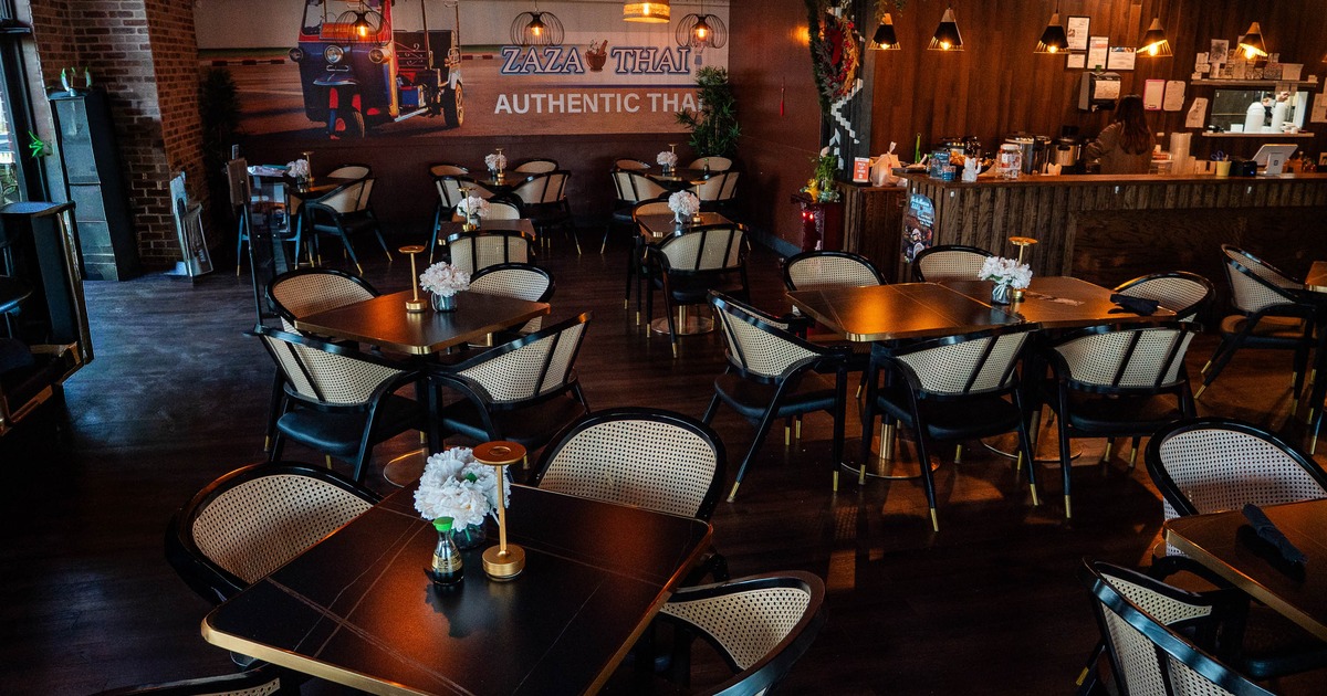 Interior of a Thai restaurant with tables, rattan chairs, a Thai mural, and counter area with pendant lights