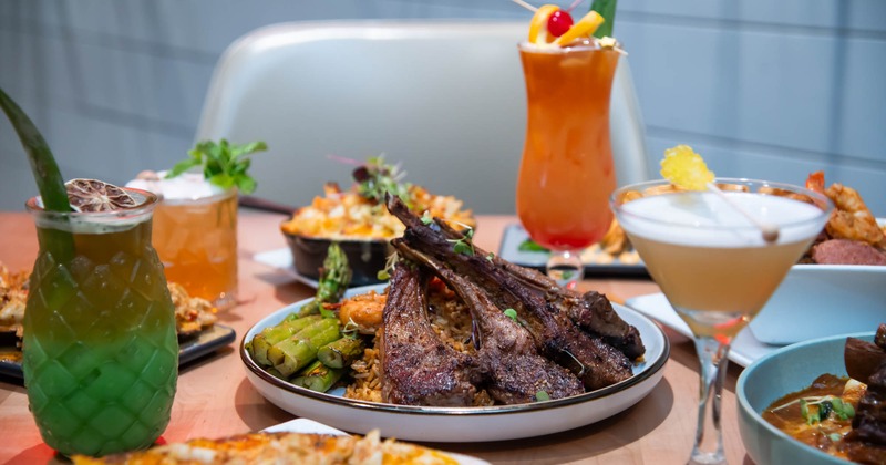 A table with an assortment of dishes and cocktails, with lamb chops as centerpiece