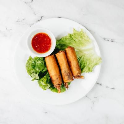 Shrimp Egg Rolls served over lettuce on a white plate with a small cup of sweet chili sauce.