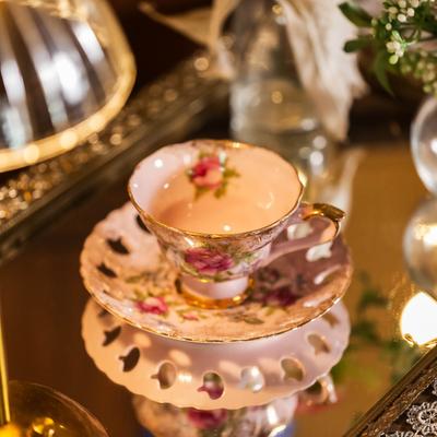 A floral teacup with a saucer on a reflective surface.
