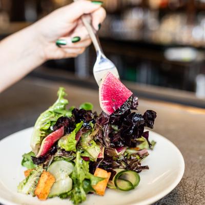 a hand takes a forkful of Supra's spring salad with radish, lettuce greens etc