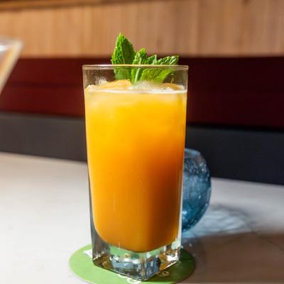 A tall glass of orange juice with mint leaves on a green coaster.