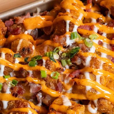 Loaded Tater Tots, with sour cream, bacon, cheese, scallions, and spicy mayo.