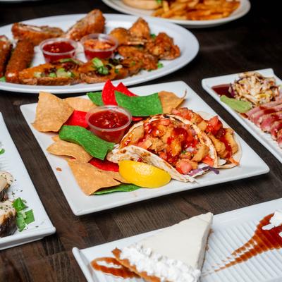 Colorful spread of dishes including fish tacos with tortilla chips, tuna tataki, and cheesecake.