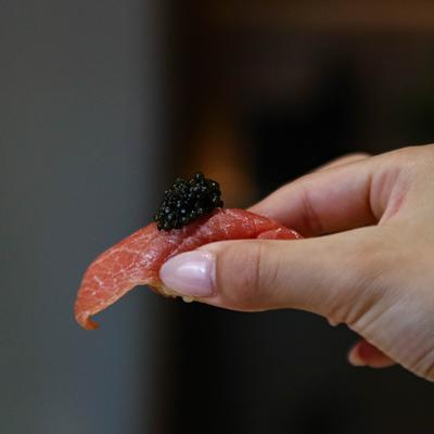 A hand holding a tuna slice with caviar.