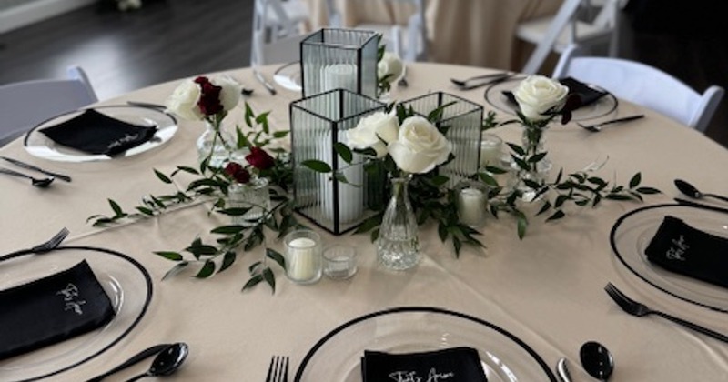 Round table set with plates, candles, white roses, and greenery