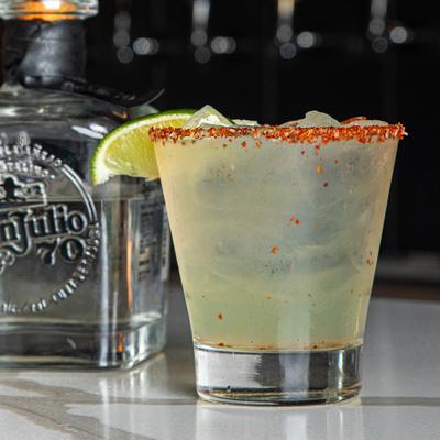 Margarita garnished with a chili rim and a lime wedge, alongside a bottle of tequila.
