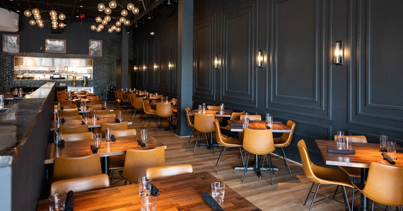 Interior with wooden tables, tan leather chairs, and exposed bulb lighting