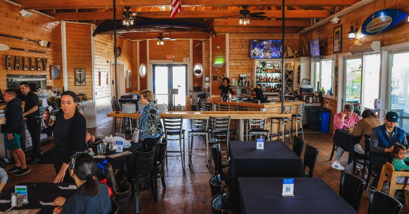 Interior, diner area, tables, chairs, stuff, guests, bar behind, tv screens above