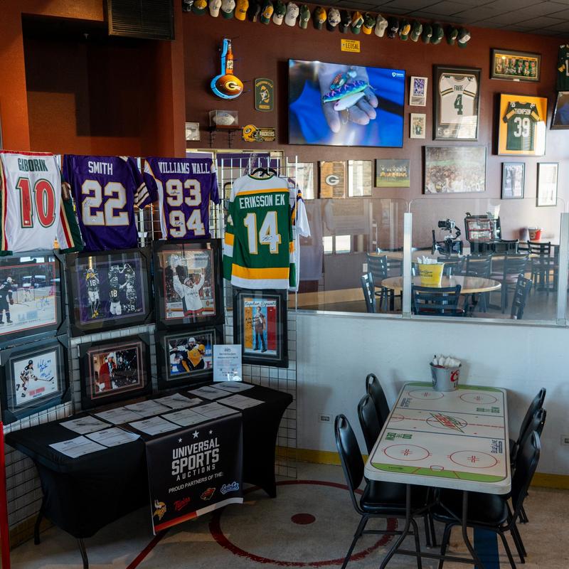 Sports-themed bar interior with jerseys, framed sports memorabilia, and dining tables