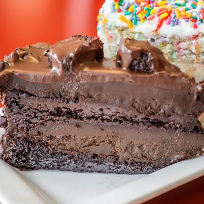 Chocolate fudge cake slice next to a colorful sprinkle cake.